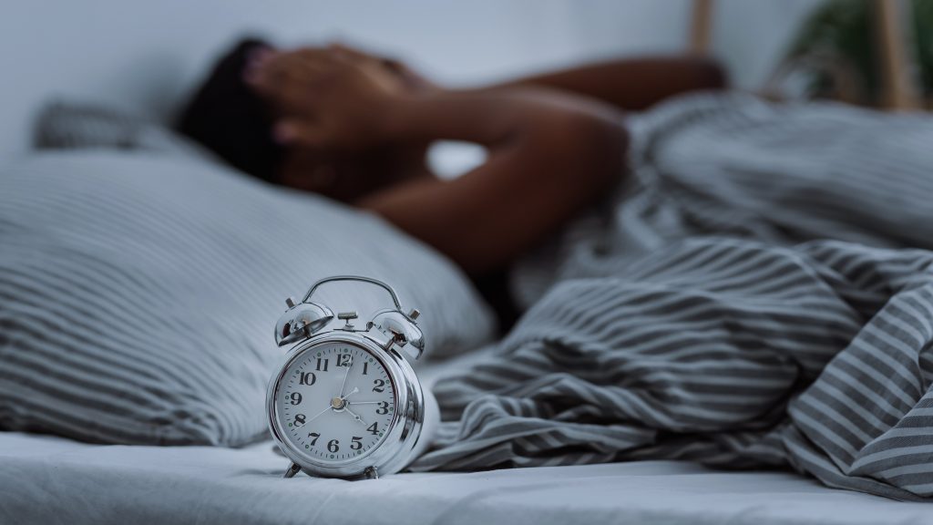 Image of a person in bed with a clock in the foreground